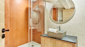 Un bagno moderno con doccia vetrata, specchio rotondo e mobile vanitario in legno con lavandino.