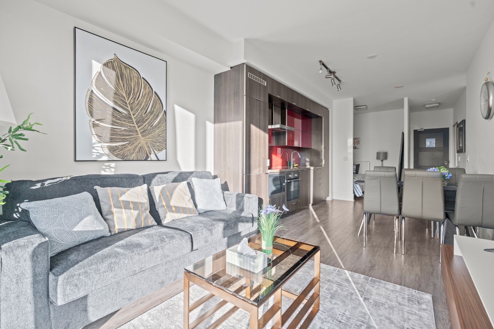 A modern living room with a grey sofa, a glass coffee table, and a dining area with a grey table and chairs.