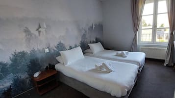 Ein Hotelzimmer mit zwei Betten, einem Nachttisch und einem Fenster mit Vorhängen.