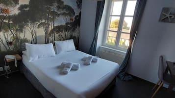 Un lit bien fait, avec du linge de lit et des serviettes blanches, une table de chevet avec un téléphone, une fenêtre avec des rideaux et une fresque représentant des arbres sur le mur.