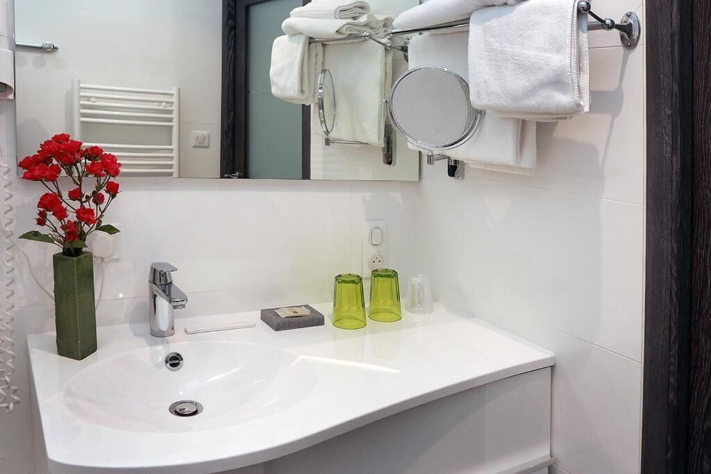 Un baño con un lavabo blanco, un espejo, un perchero con toallas dobladas y un florero con flores rojas.