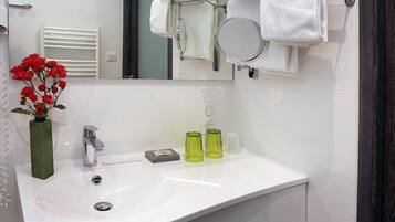 Un baño con un lavabo blanco, un espejo, un perchero con toallas dobladas y un florero con flores rojas.
