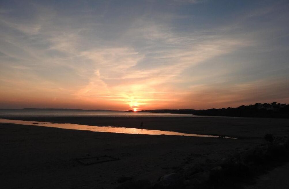 Une plage au coucher du soleil, avec une mer calme et un ciel dégagé.