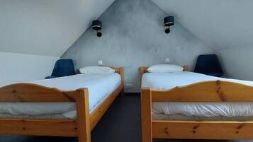 Duas camas de madeira com lençóis brancos em um quarto com teto inclinado e parede em tom claro.