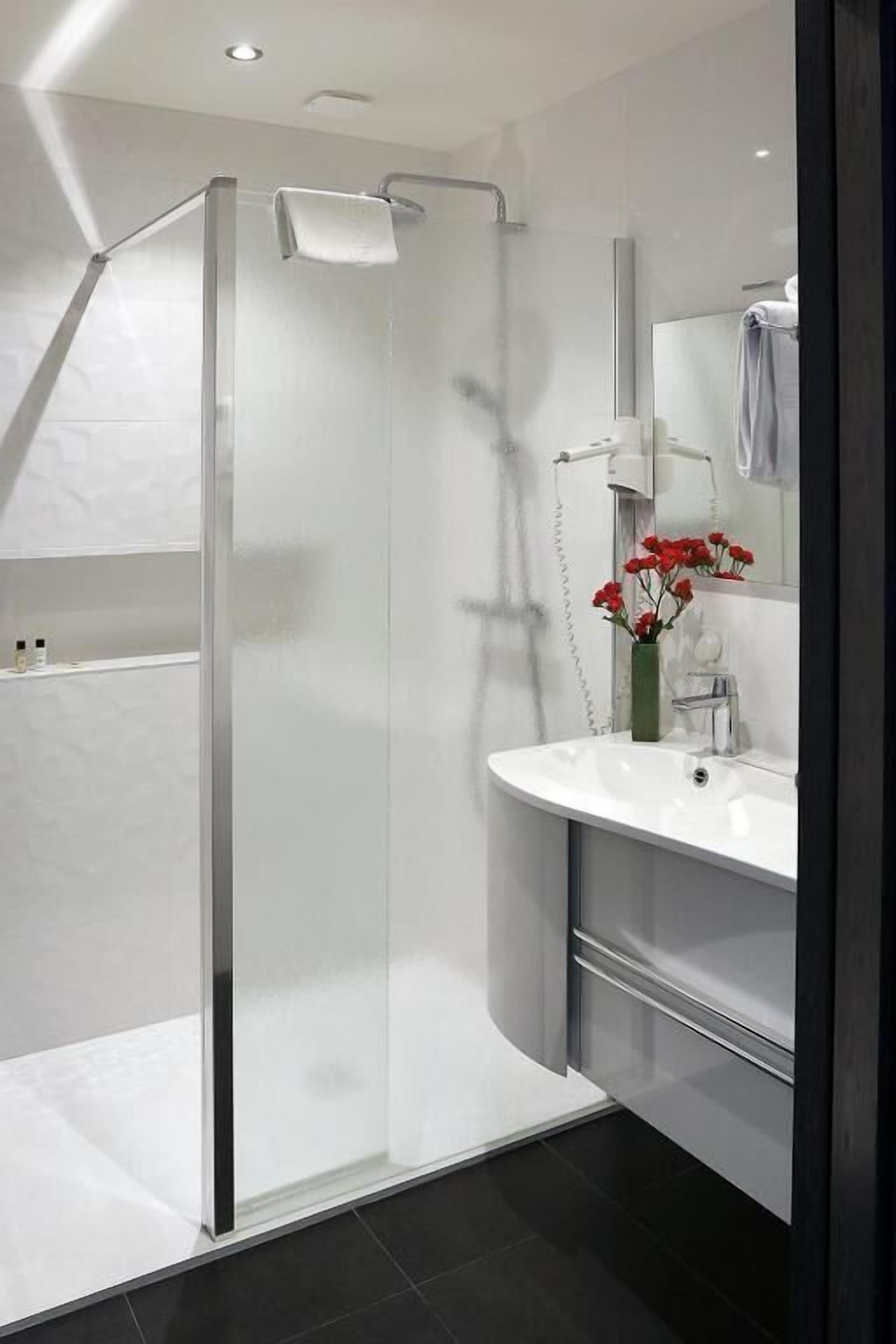 A modern bathroom with a glass-enclosed shower, a white sink, and a mirror above it.