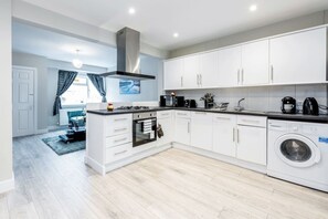 Una cocina moderna con armarios blancos, horno empotrado, estufa, lavadora y comedor con mesa y sillas.