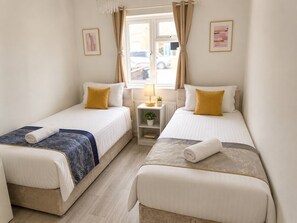 Una habitación de hotel con dos camas, una mesita con lámpara y una ventana con cortinas.