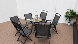 Une terrasse avec une table ronde, six chaises et une bouteille de spiritueux.