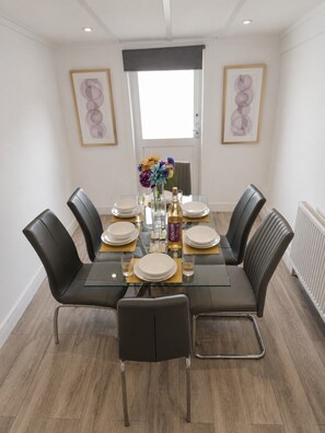 Comedor con una mesa de vidrio, seis sillas y un jarrón con flores.