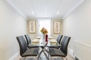 Comedor con una mesa de vidrio, sillas negras y un florero con flores.