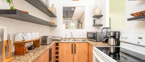 A modern kitchen with granite countertops, wooden cabinets, a built-in oven, a microwave, and a coffee maker.