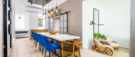 A modern dining area with a white table, blue chairs, and wicker chairs.