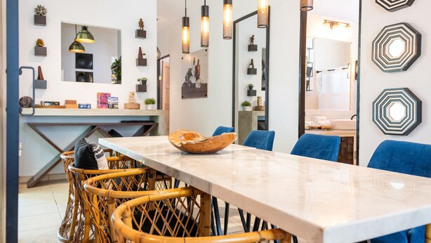 Un'elegante zona pranzo moderna con tavolo in marmo, sedie in vimini, illuminazione a sospensione e decorazioni murali.