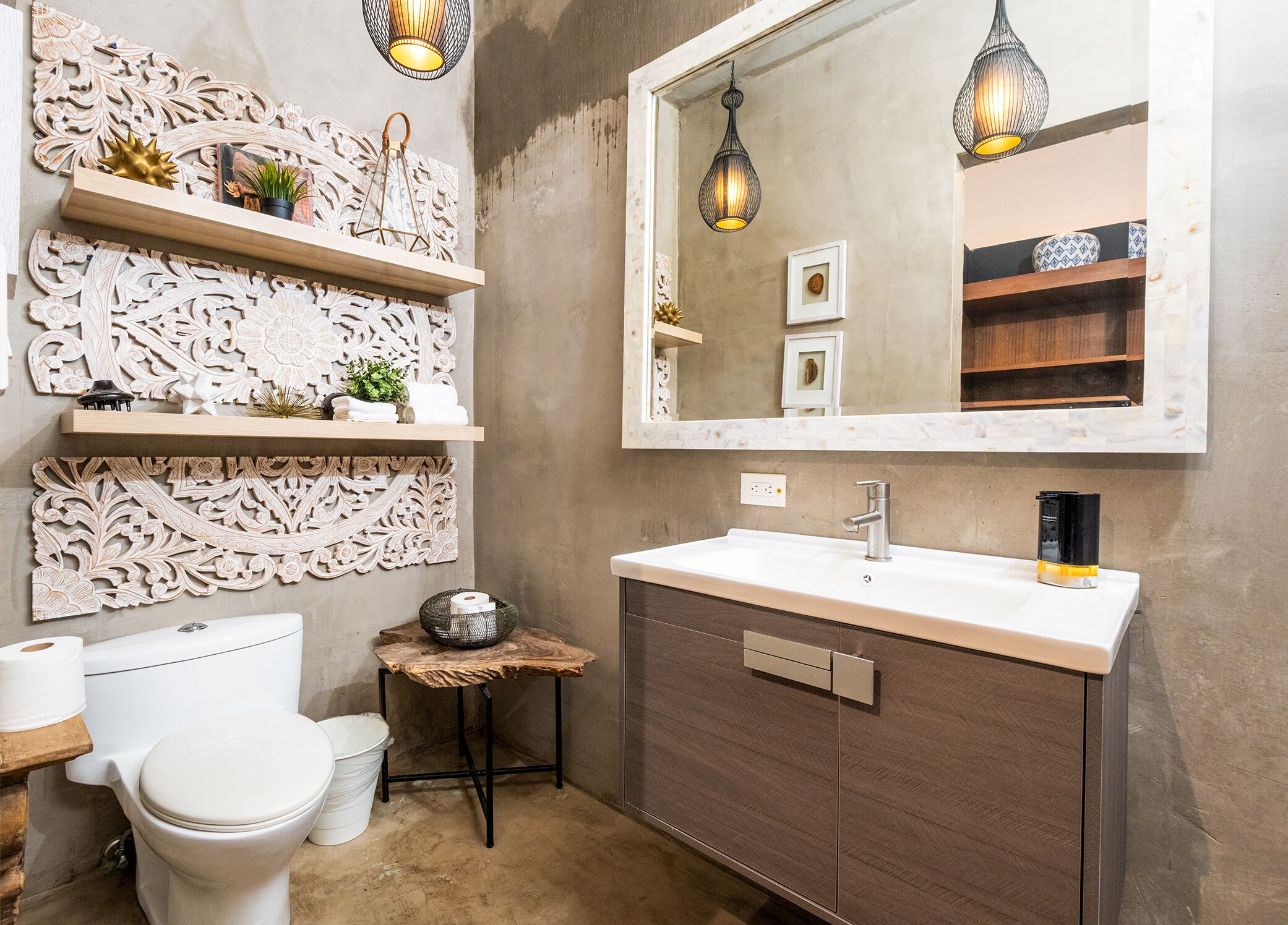 A bathroom with a toilet, sink, decorative wall panels, and a mirror with pendant lights.