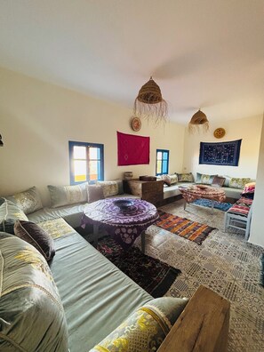 A living room with a sofa, a round table, a coffee table, and patterned rugs. - Sunrise Camp Mirleft (Mirleft)