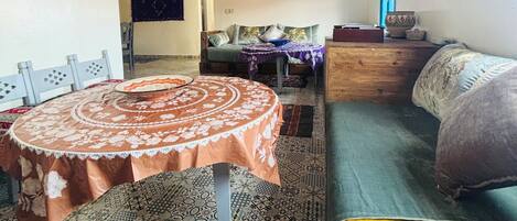 A living room with a round table, sofa, patterned rugs, and a television on the wall.