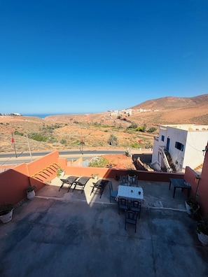 A rooftop terrace with outdoor seating, a view of the coastline, and a hilly landscape in the background. - Sunrise Camp Mirleft (Mirleft)