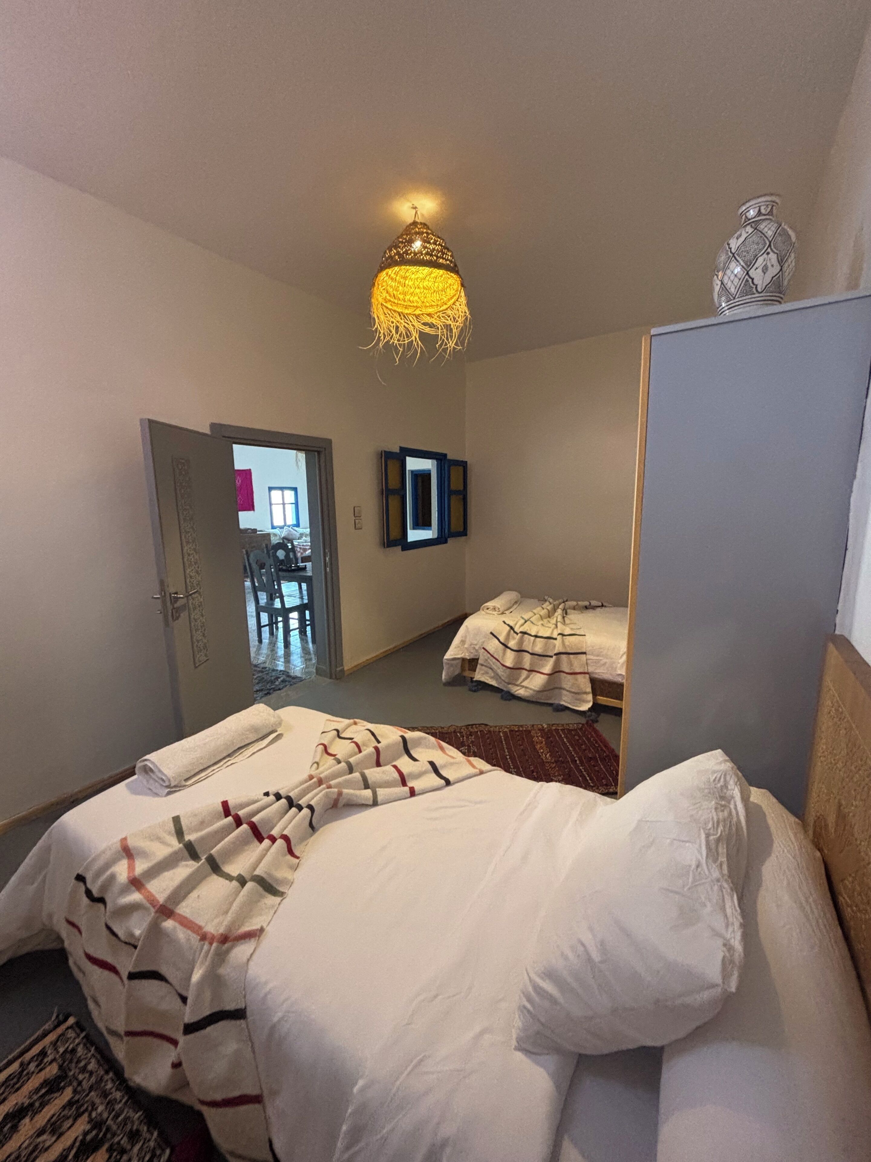 A hotel room with a bed, a mirror, a door leading to a hallway, and a chandelier.