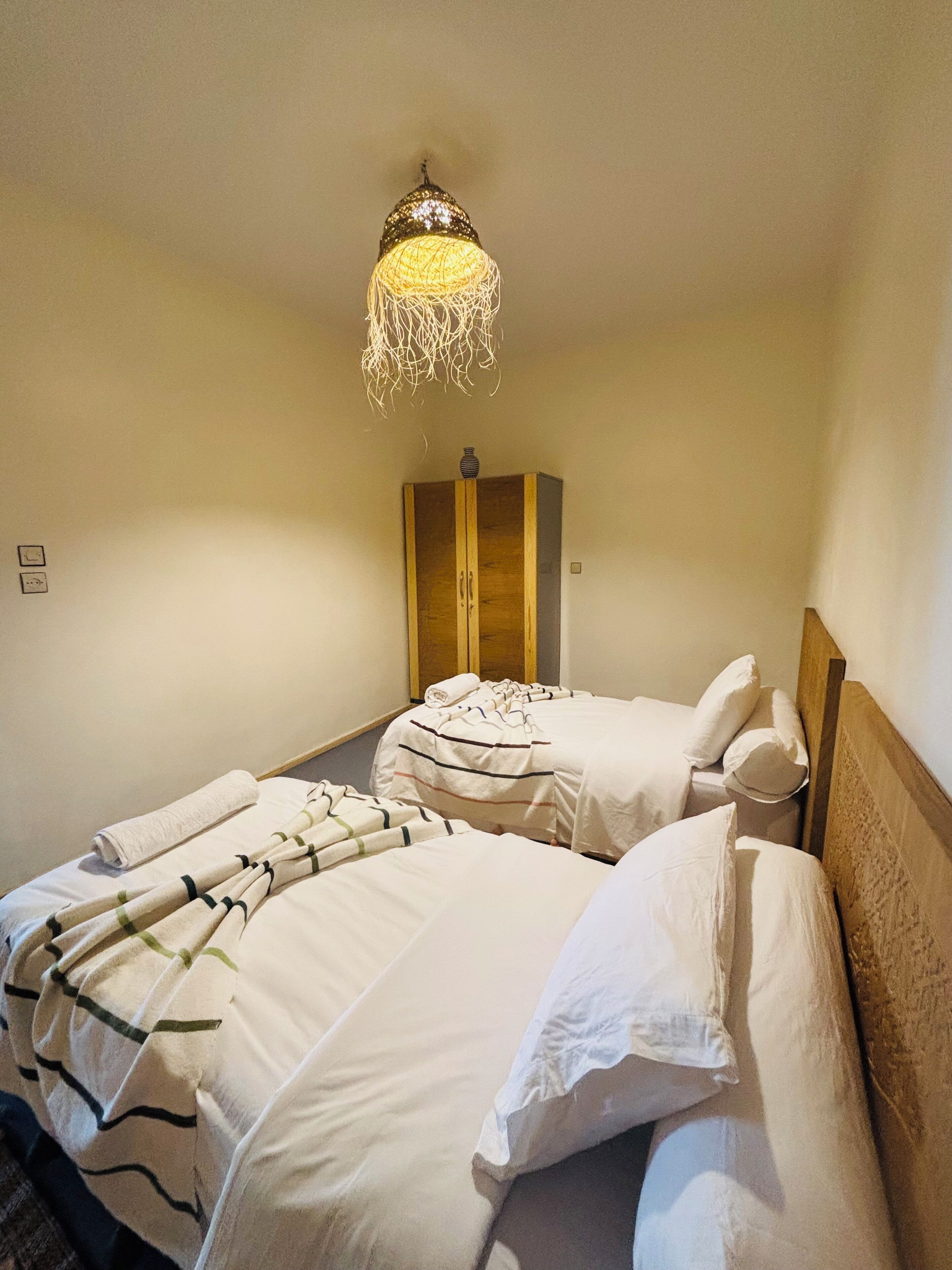 Una habitación de hotel con dos camas, un armario de madera y una lámpara colgante.