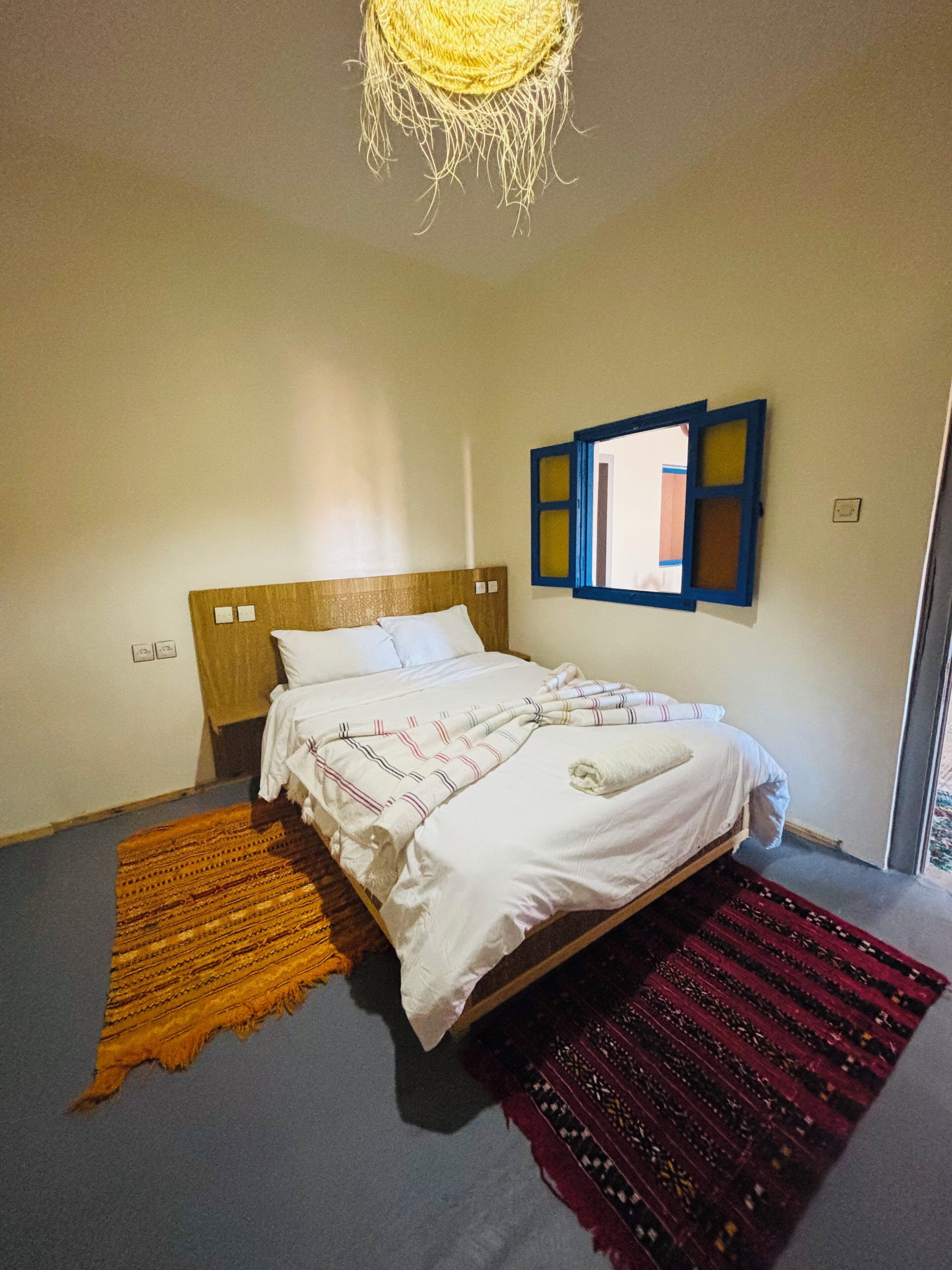 A bedroom with a bed, a hanging light fixture, a wall-mounted mirror, and two rugs.