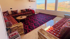 Ein Wohnzimmer mit einer Sofagarnitur, einem Couchtisch, einem gemusterten Teppich und Blick auf eine Wüstenlandschaft durch große Fenster.