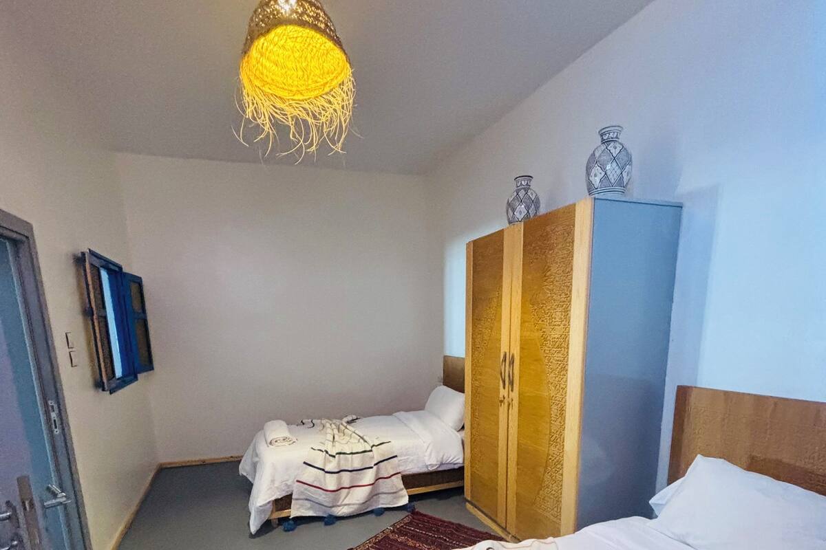 A hotel room with two beds, a wardrobe, a television, and a hanging light fixture.