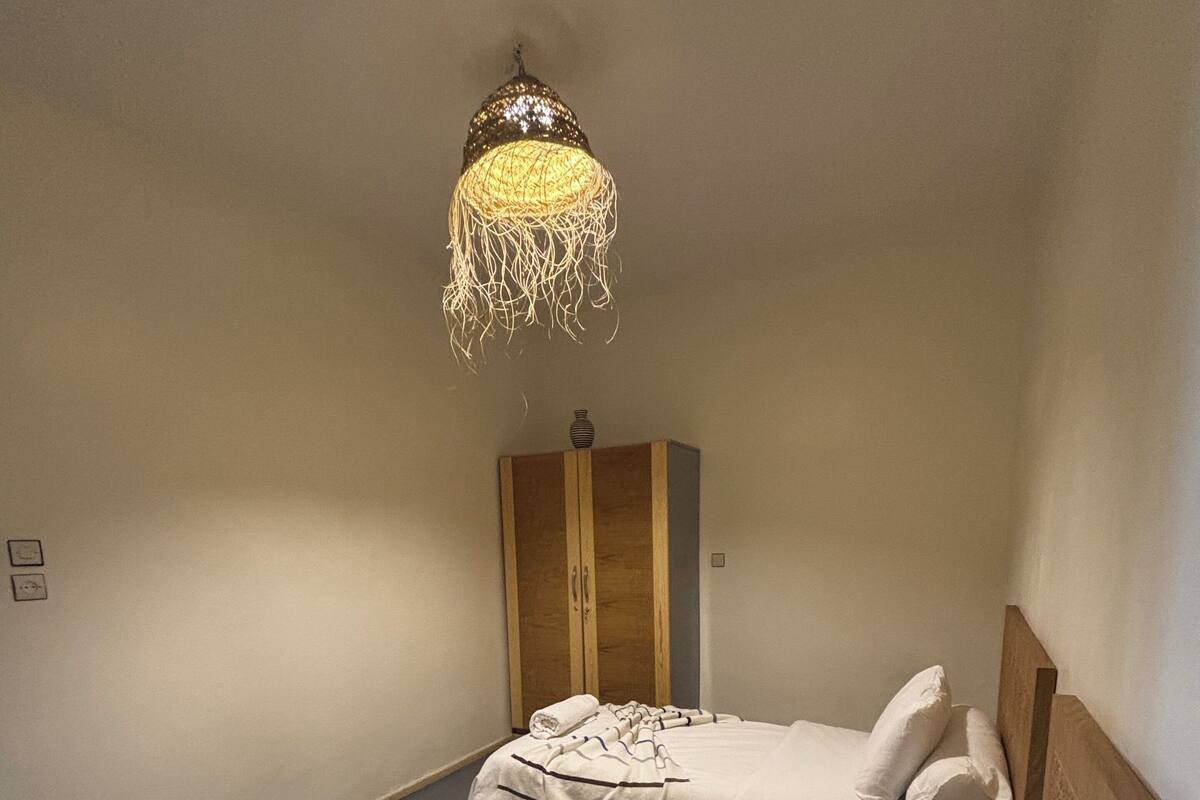 A bedroom with two beds, a wooden wardrobe, and a hanging light fixture.
