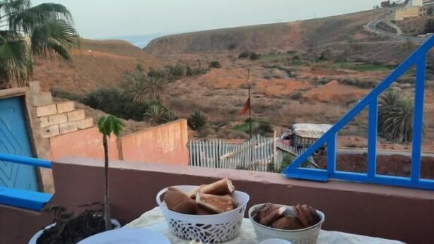 Ein Esstisch, gedeckt mit Brot, Kaffee und Gewürzen, mit Blick auf eine schöne Landschaft mit Hügeln und einem blauen Geländer.