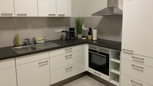 A modern kitchen with white cabinets, a stainless steel sink, a coffee maker, and an oven. - Meeresbrise 1 Top location with garden use. Pet friendly! (Tönning)