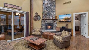 A cozy living room with a stone fireplace, comfortable seating, and a television. - Juniper Presents: Lodge Retreat w Hot Tub,Firepit,Foosball,BBQ&POOL (New Buffalo)