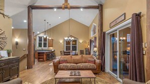 A spacious living room with a large sofa, a coffee table, and a dining area in the background. - Juniper Presents: Lodge Retreat w Hot Tub,Firepit,Foosball,BBQ&POOL (New Buffalo)
