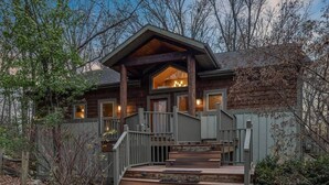 A log cabin with a porch, wooden steps, and a view of the surrounding forest. - Juniper Presents: Lodge Retreat w Hot Tub,Firepit,Foosball,BBQ&POOL (New Buffalo)