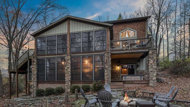 A two-story house with a stone facade, large windows, a balcony, and outdoor seating. - Juniper Presents: Lodge Retreat w Hot Tub,Firepit,Foosball,BBQ&POOL (New Buffalo)