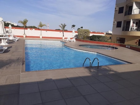 Una piscina al aire libre, sombrillas, sillones reclinables de piscina