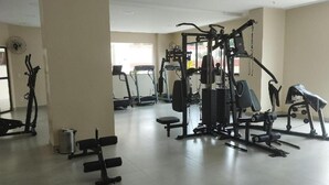 A gym with various exercise machines, a bench, and a fan on the wall.