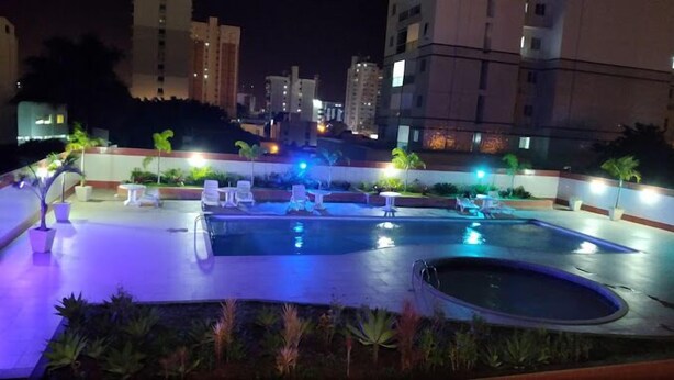 A rooftop pool area with lounge chairs and a hot tub, surrounded by potted plants and illuminated by ambient lighting.