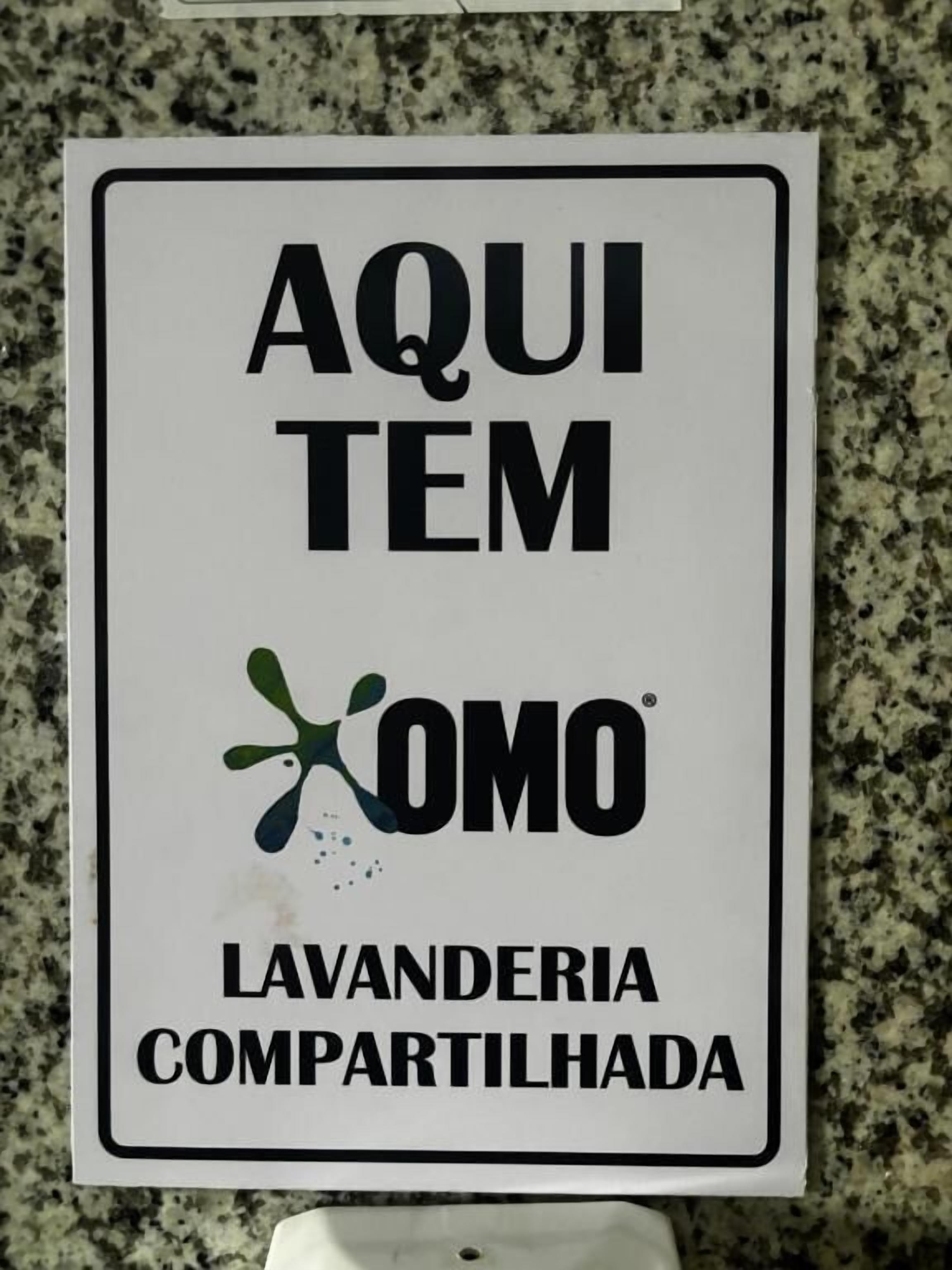 Une enseigne avec le texte « AQUI TEM LAVANDERIA COMPARTILHADA » et un logo.