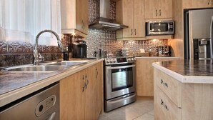A modern kitchen with stainless steel appliances, wooden cabinets, and a tiled backsplash. - Beautiful home for you (Sherbrooke)