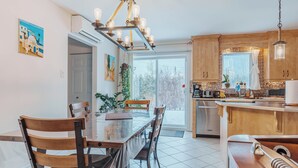 A modern kitchen with wooden cabinets, a dining table with chairs, and a large window providing a view of the outdoors. - Beautiful home for you (Sherbrooke)
