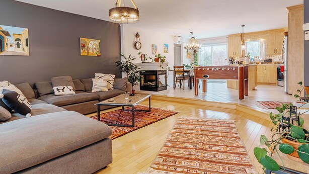 A modern living room with a sofa, coffee table, and a fireplace. There is a dining area with a table and chairs, and a kitchen in the background. - Beautiful home for you (Sherbrooke)