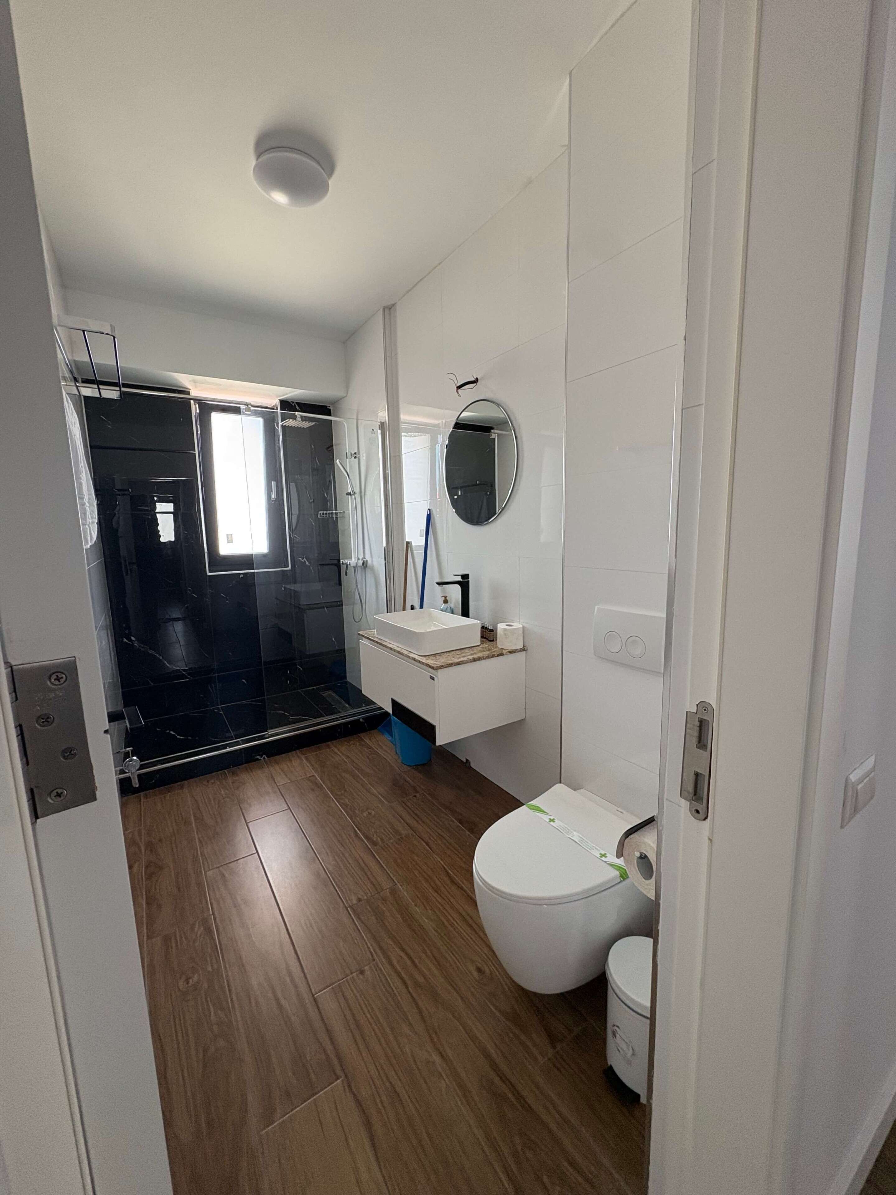 A bathroom with a toilet, sink, mirror, and shower area.