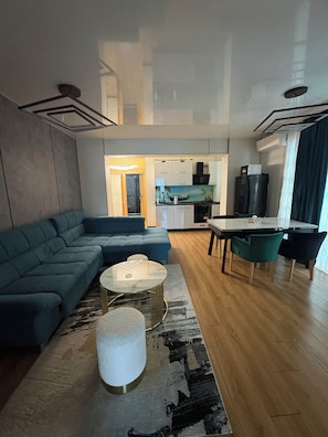 A modern living room with a sectional sofa, a round coffee table, and a dining area with a table and chairs. - Signature Promenada Hotel-Apartments 2 (Navodari)