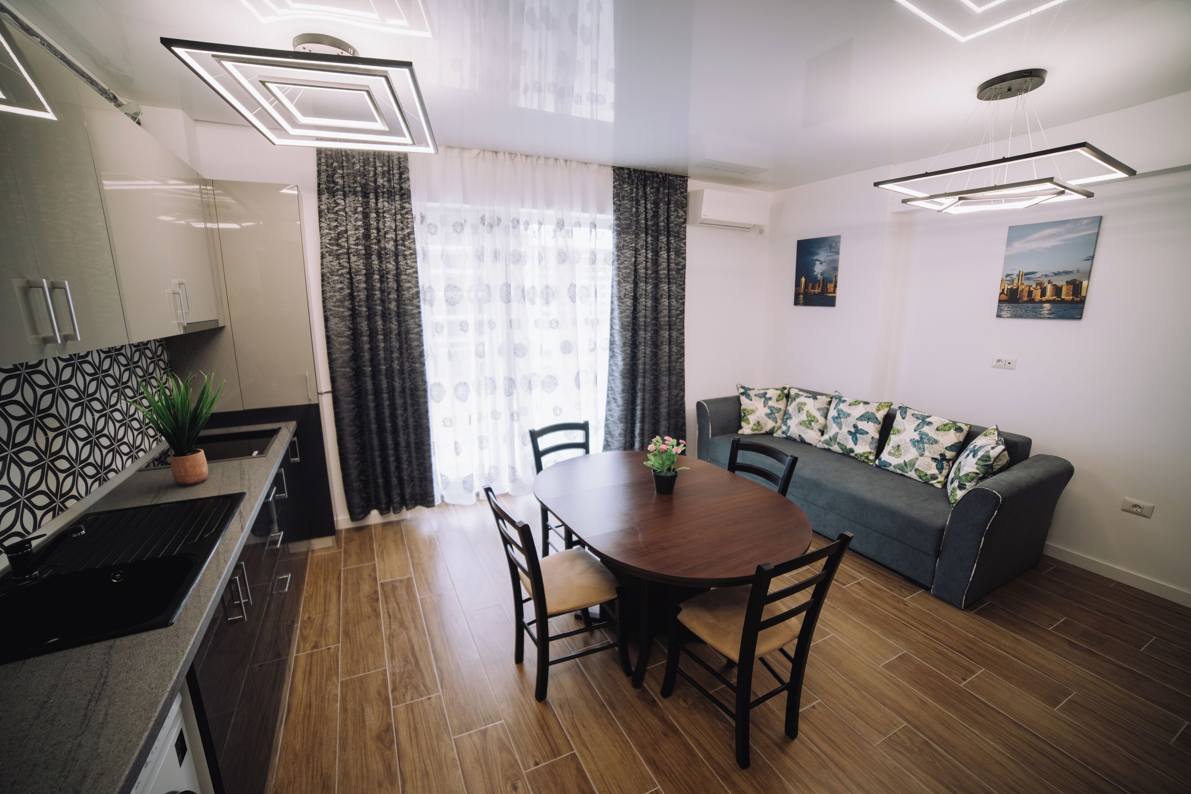 A modern kitchen with a dining area, a sofa, and a cityscape painting on the wall.