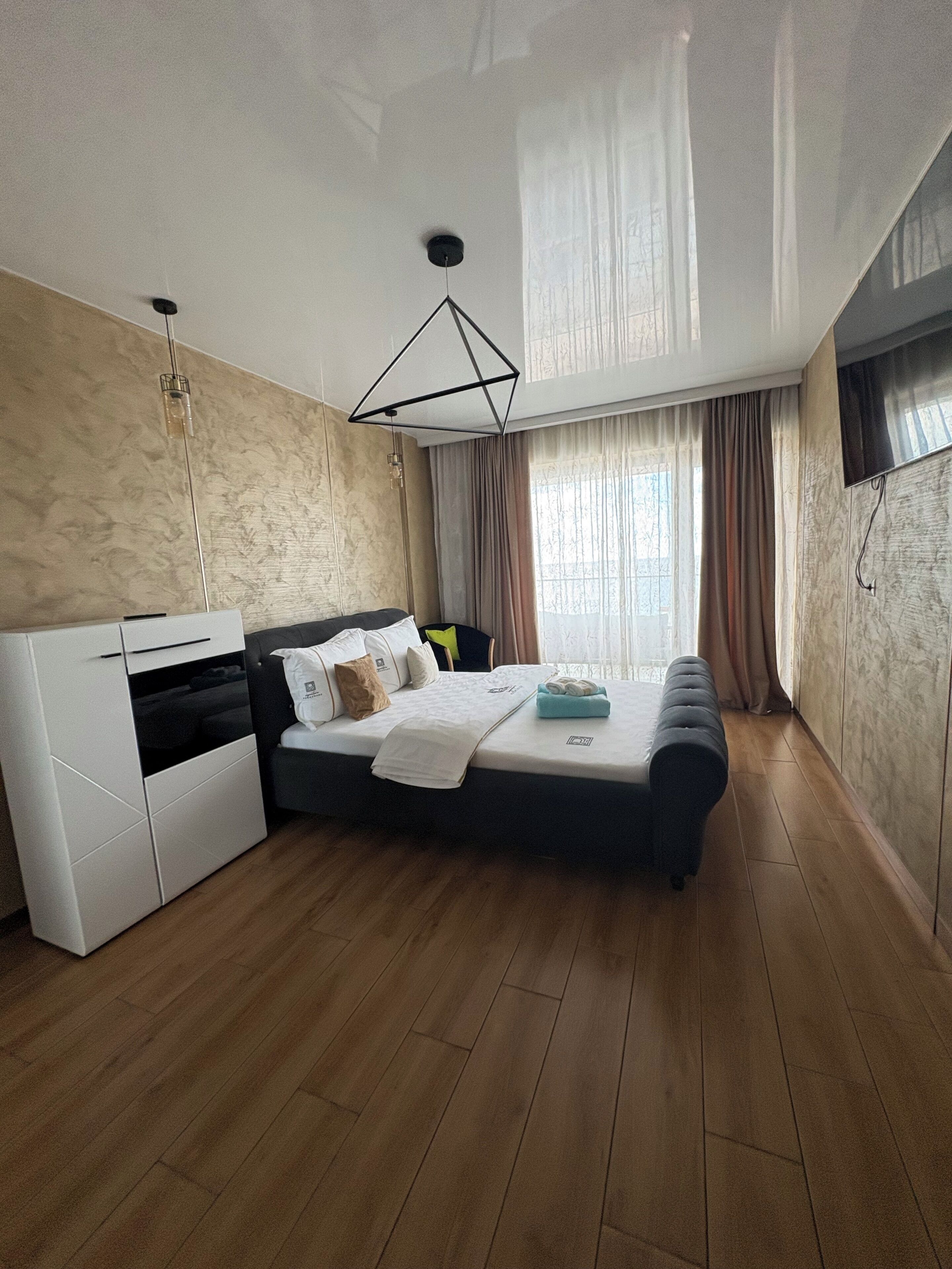 A modern bedroom with a bed, a wardrobe, a desk, and a TV.