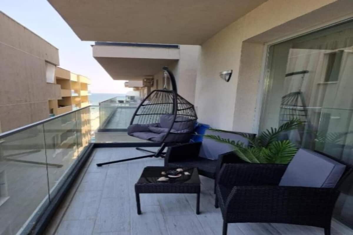 Un balcon avec un fauteuil suspendu, une petite table avec un plateau et un fauteuil en osier.