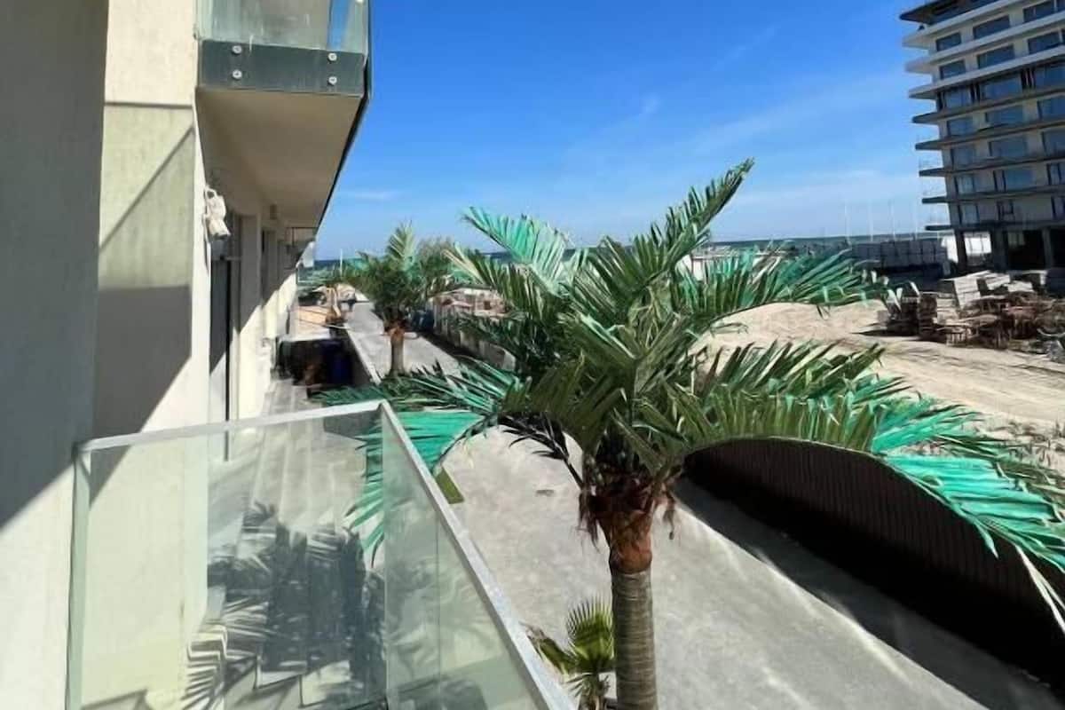 Un balcon offrant une vue dégagée sur un chantier de construction, des palmiers et un immeuble en construction.