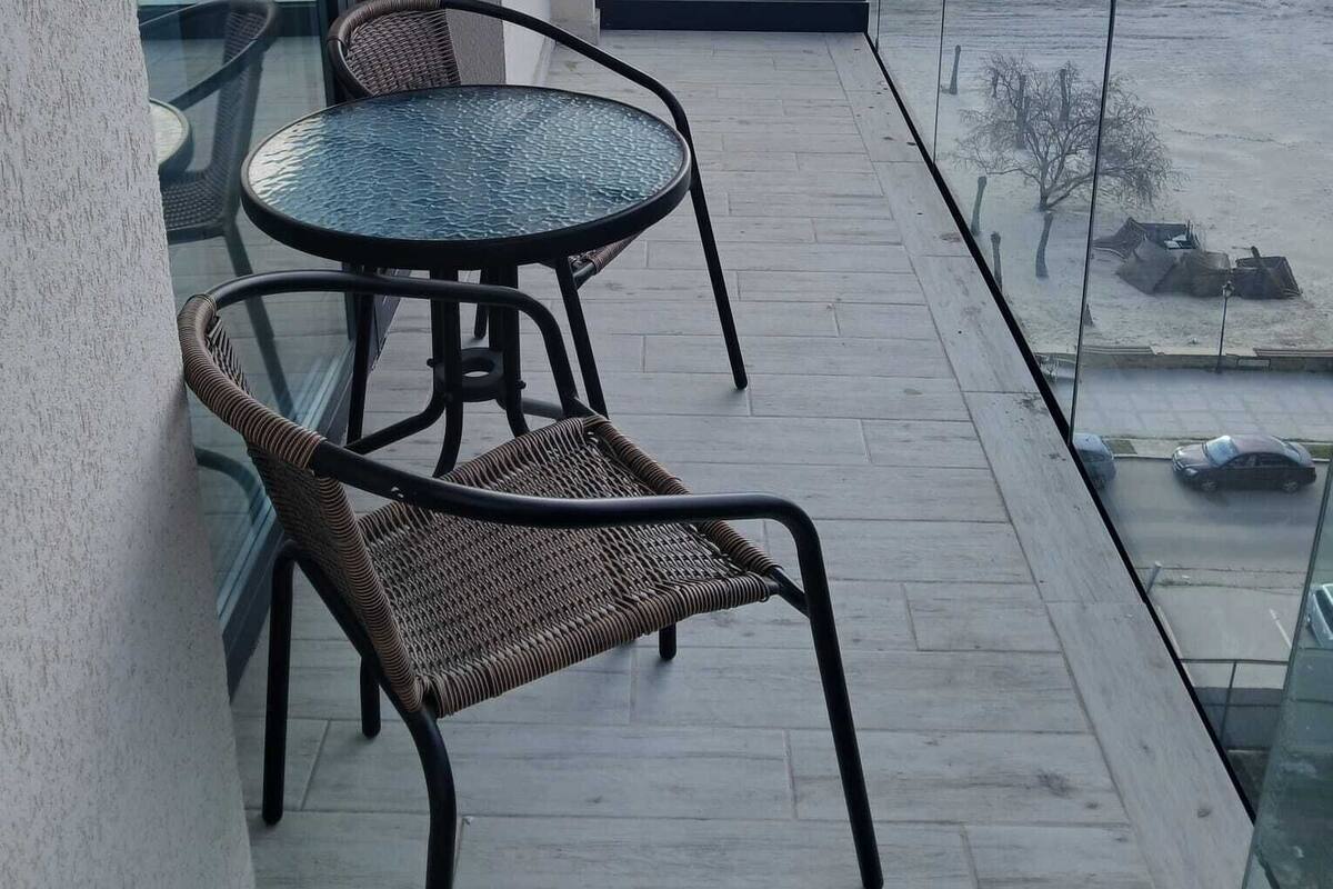 Un balcon doté d’une balustrade en verre, une table ronde, deux chaises en osier et une vue sur la plage.