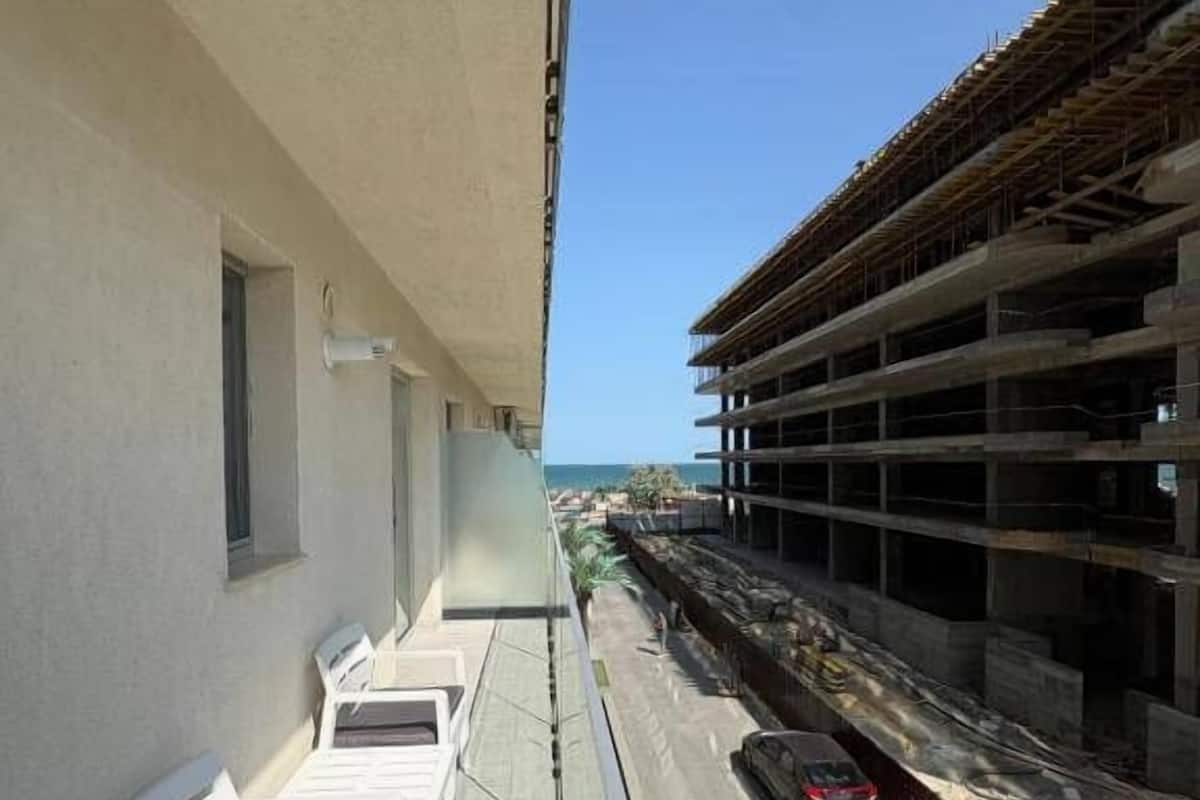 Un balcon avec des chaises blanches, une voiture blanche et un immeuble en construction.