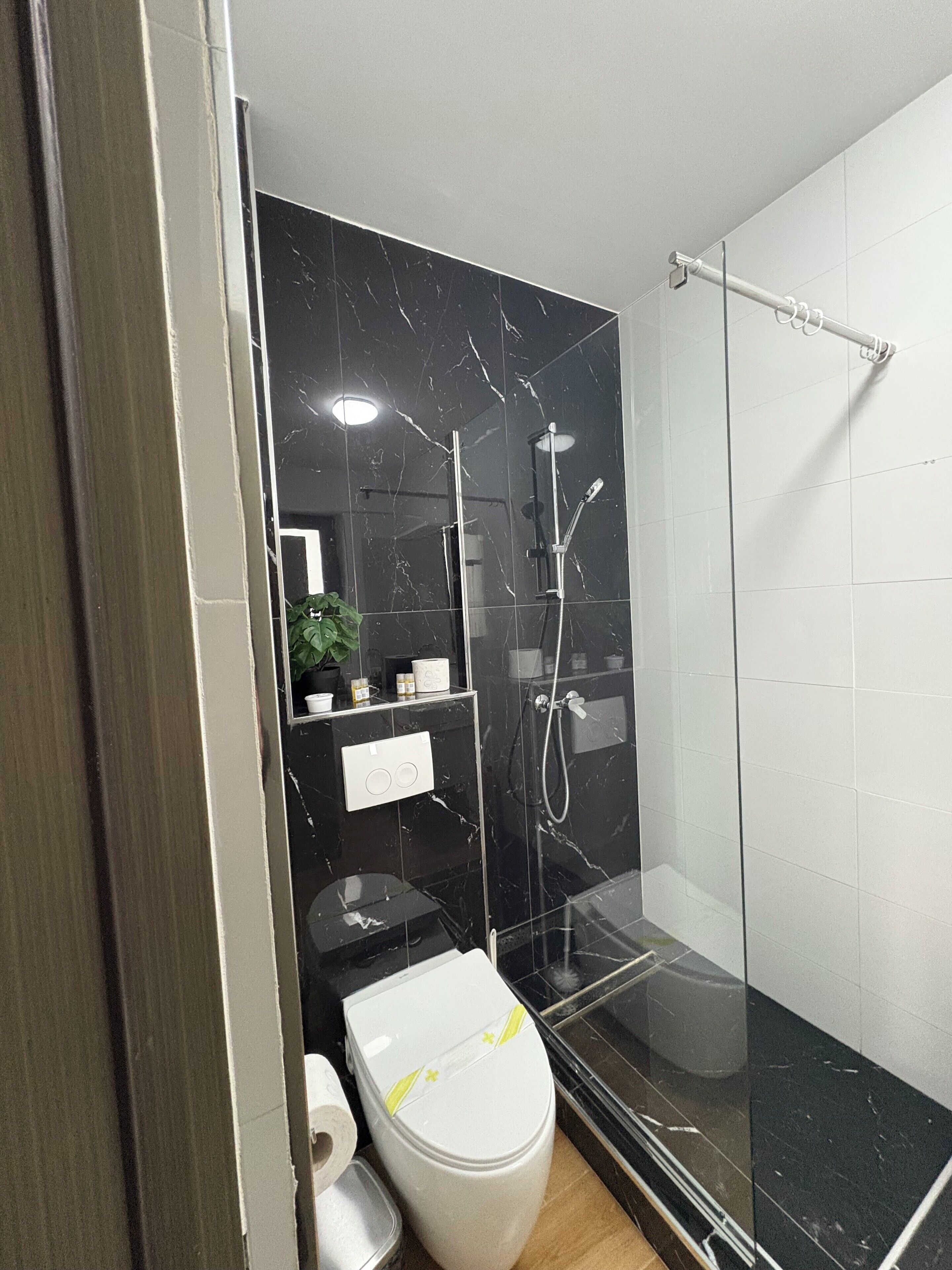 A modern bathroom with a glass-enclosed shower, a toilet, and a sink area with toiletries.