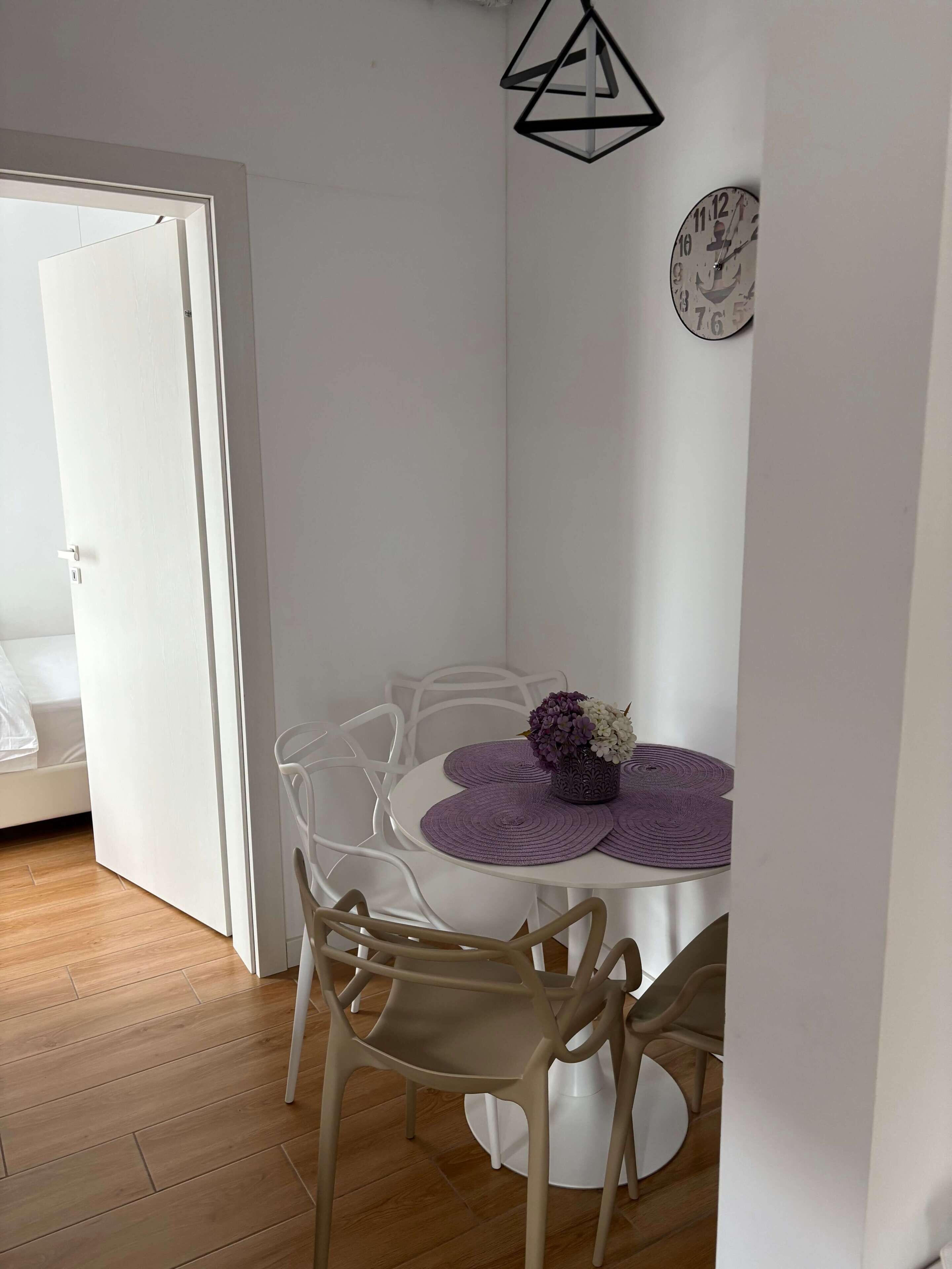 Un coin repas avec une table ronde, des chaises blanches et des sets de table violets.